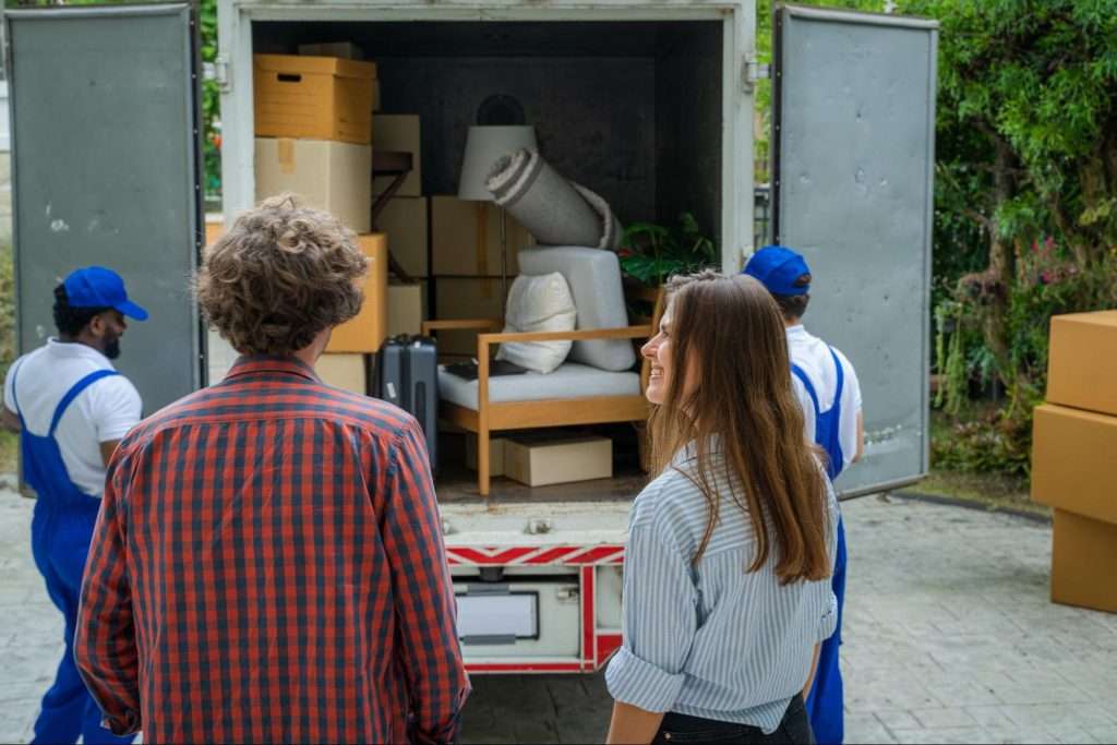 Young couple smiling as they watch Canal Fulton movers load their belongings into a moving truck. 
