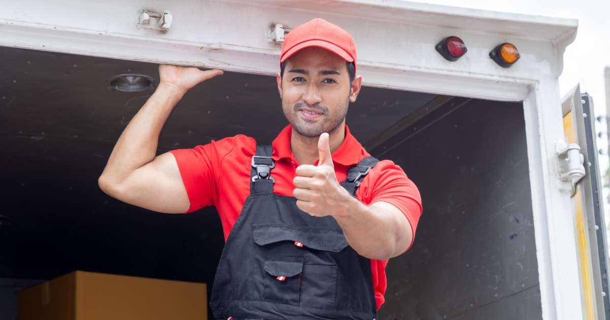 Summit Moving mover standing on the back of a moving truck and holding a hand out with a thumbs up